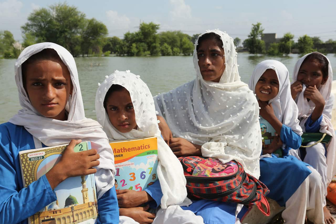 Young girls clutch their books to their chest on a boat in flooded waters. 