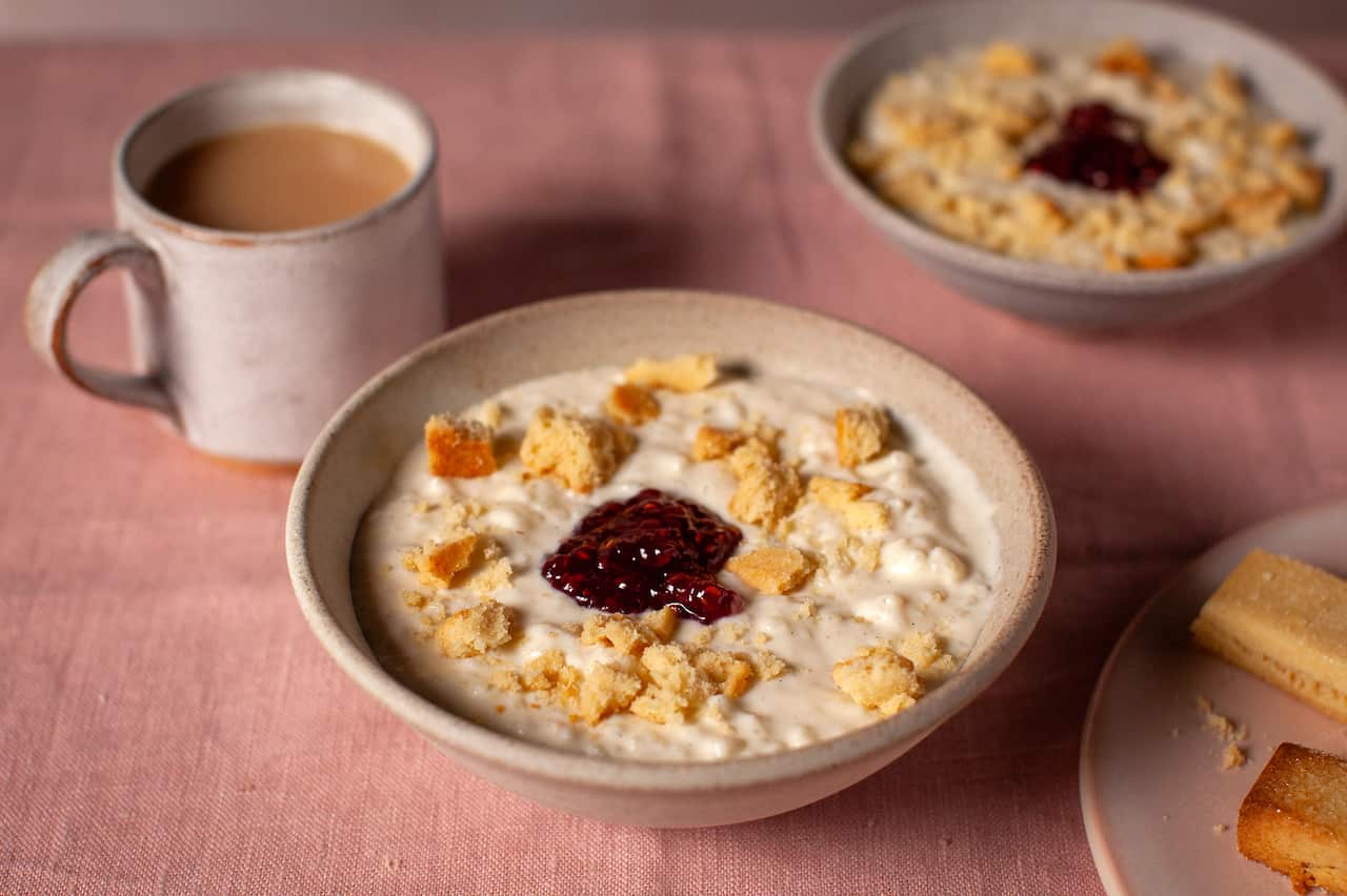 A bowl of rice pudding, topped with a dollop of jam and crumbled shortbread fingers. 