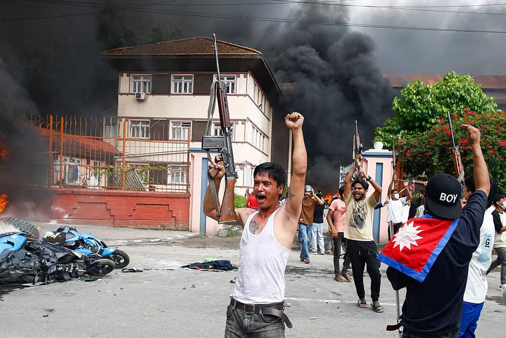 A group of protesters hold rifles up and shout in the street.
