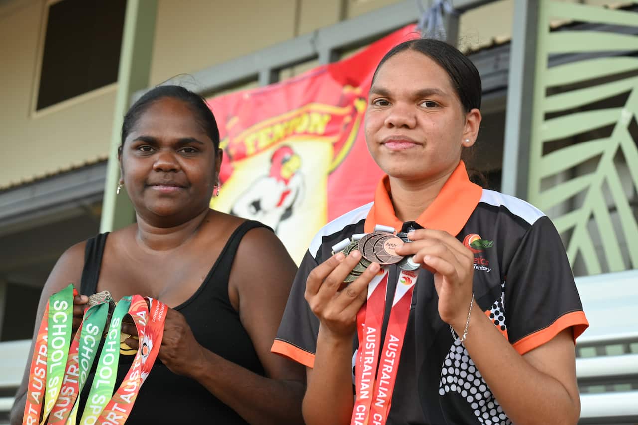 A mother and daughter stand together. Both are holding medals on ribbons
