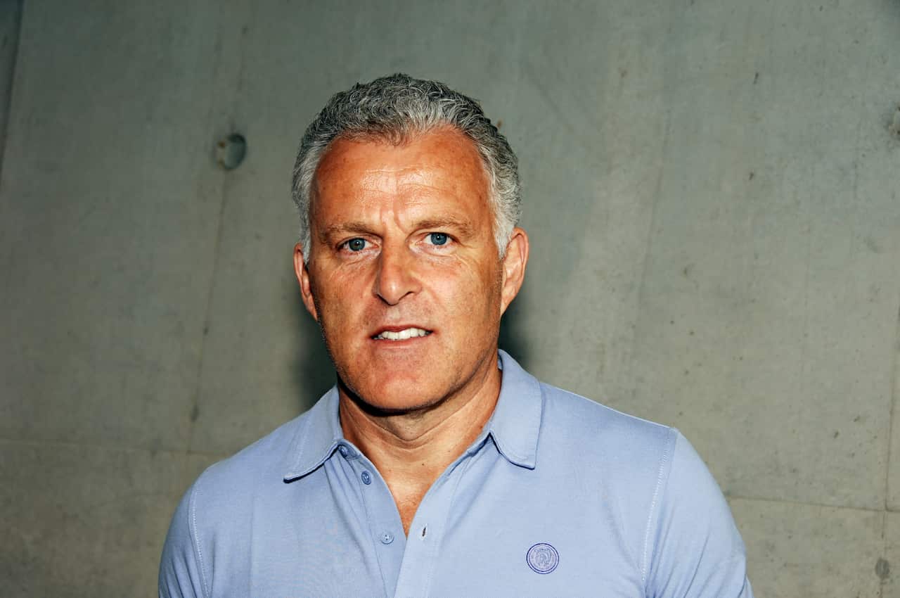A middle aged man with gray hair wearing a blue shirt 