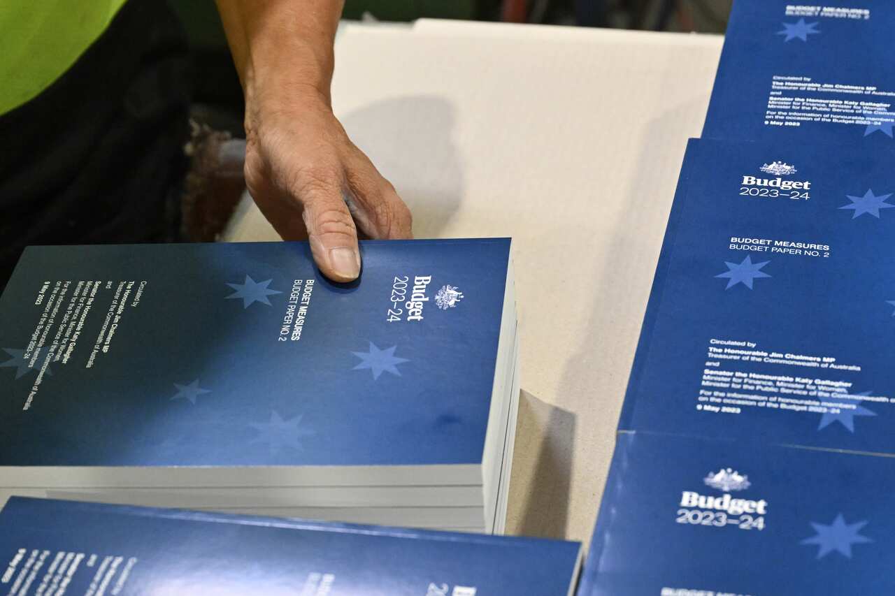 A hand holds stacks of copies of the 2023-24 budget.