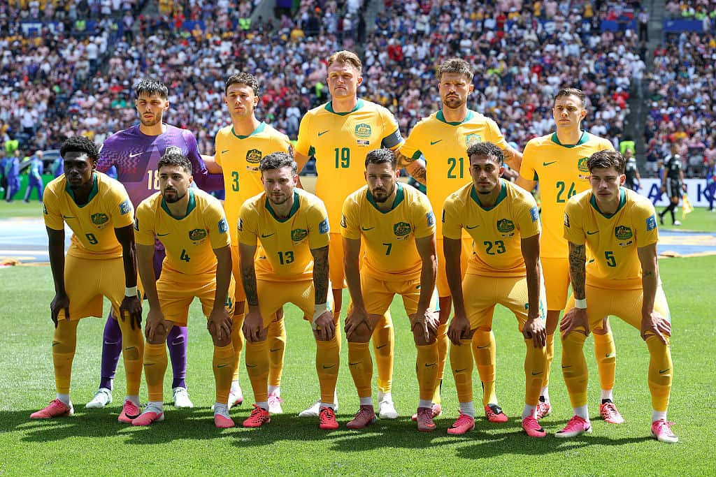 The Australian men's soccer team in yellow shirts crouching down