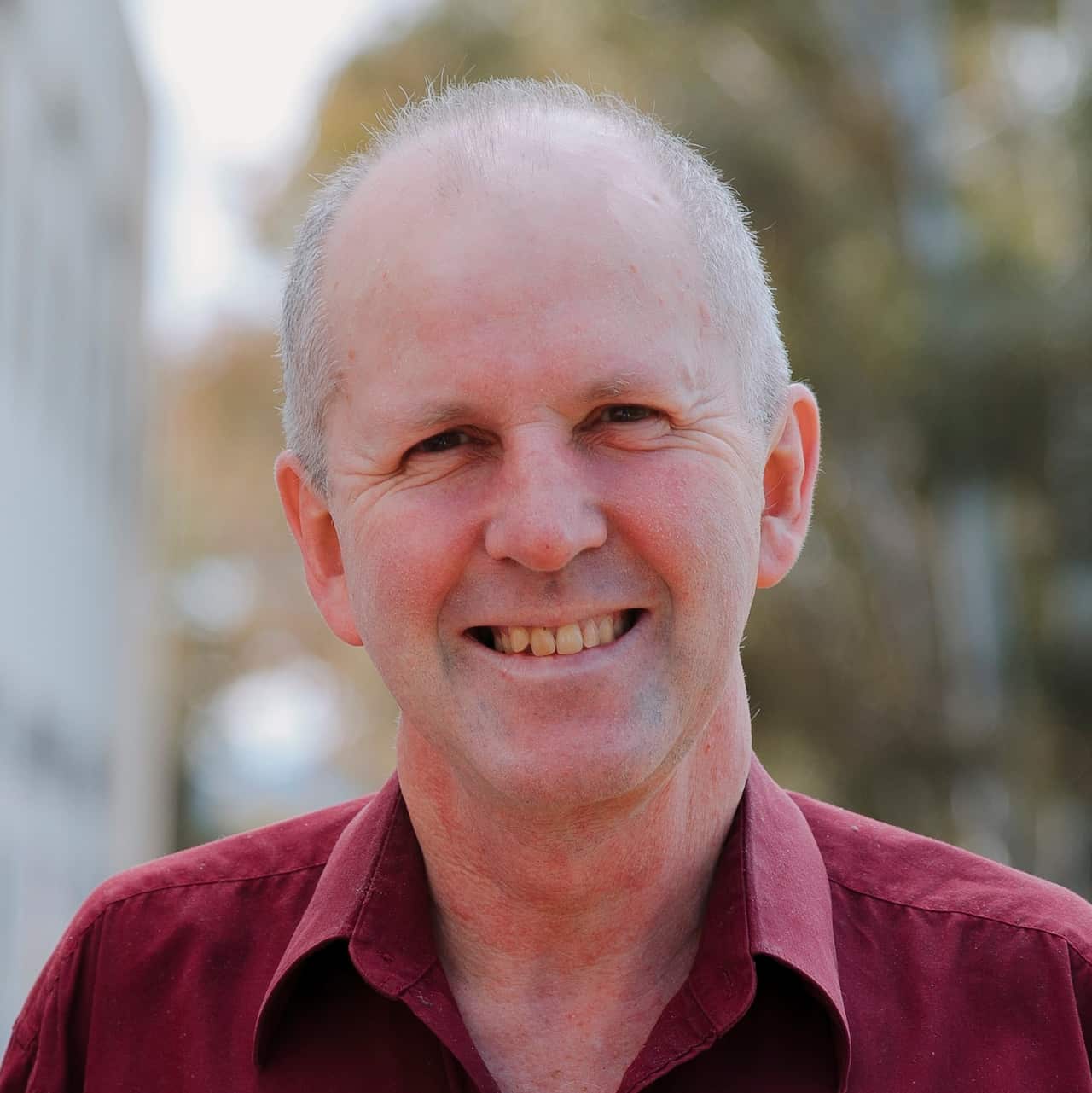A man earing a maroon collared shirt smiles and looks forward.