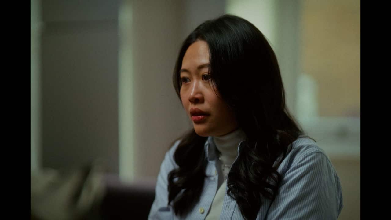 A young Asian woman with long dark hair wearing a white turtleneck and a navy blue shirt over it