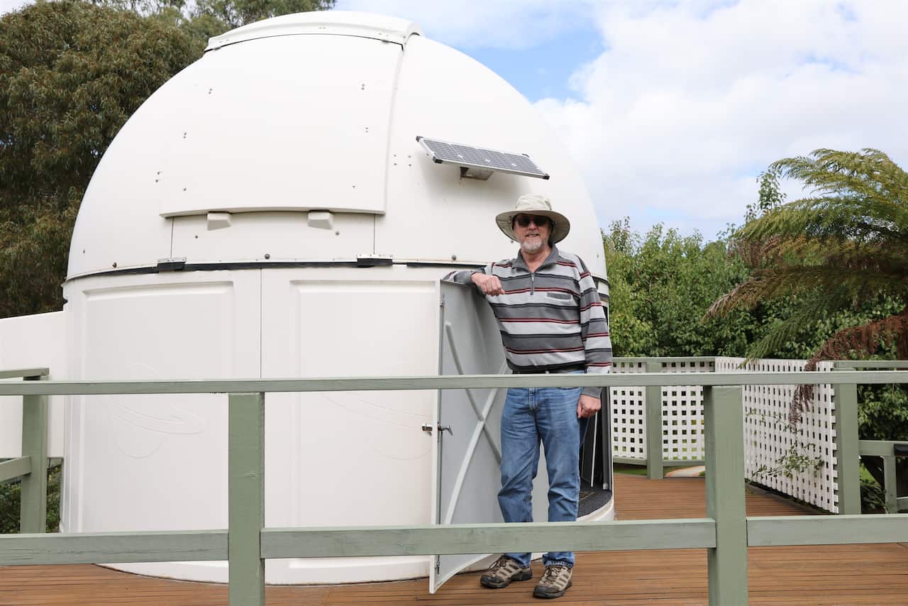 A man stands outside next to a telescope on a porch.