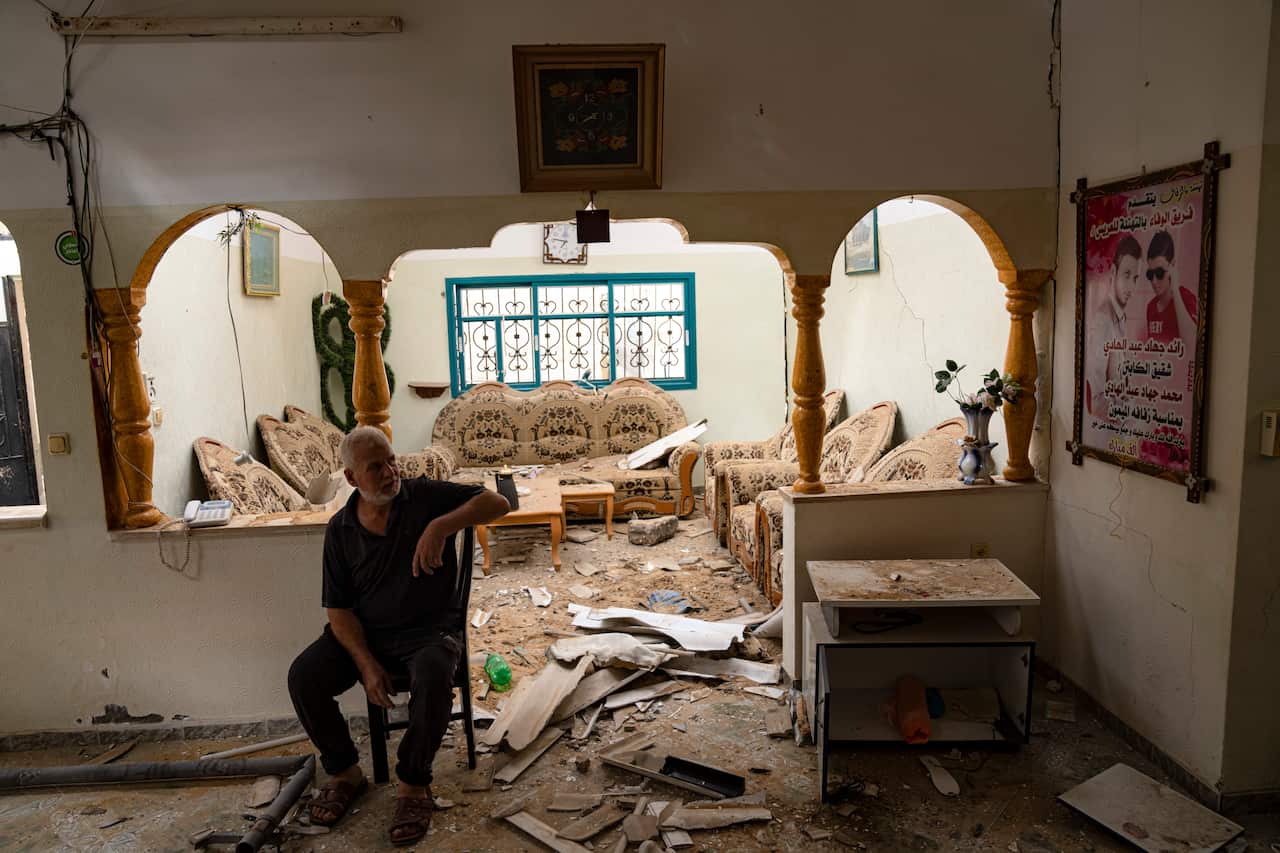 A man sits inside a home heavily damaged by bombs
