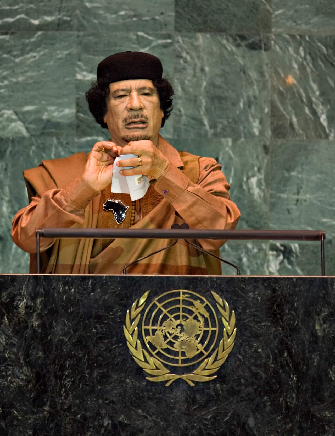 Muammar Gaddafi, wearing an orange gown, tearing up a small booklet at the United Nations General Assembly podium