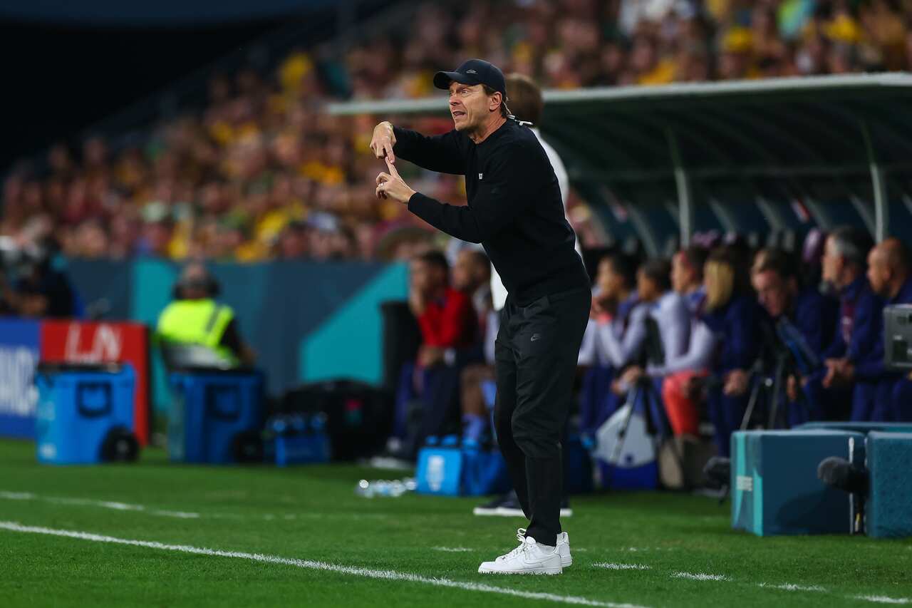 A man wearing a black tracksuit directs players at a football match.