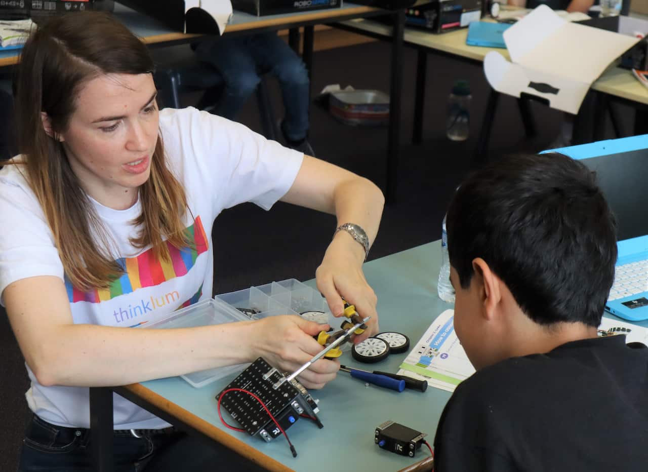 Mila Loginovski sitting at a table working on a robot while a student sits opposite and watches