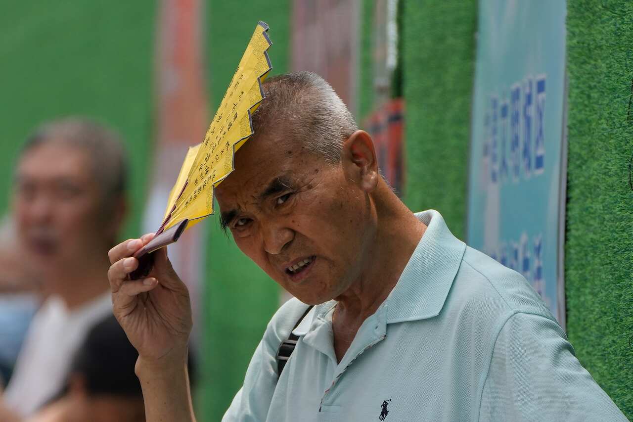 A Chinese man holding a yellow fan to his head