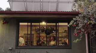 a shot of four people inside a kitchen seen from the outside through a window.
