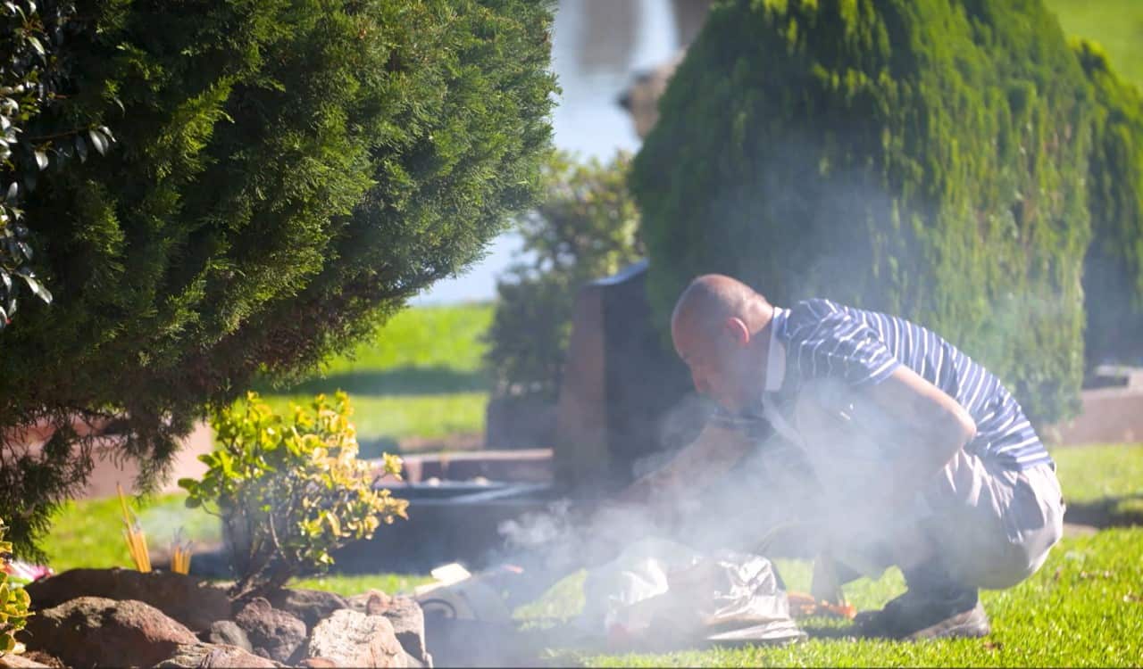 A man next to a grave surrounded by smoke from incense. 