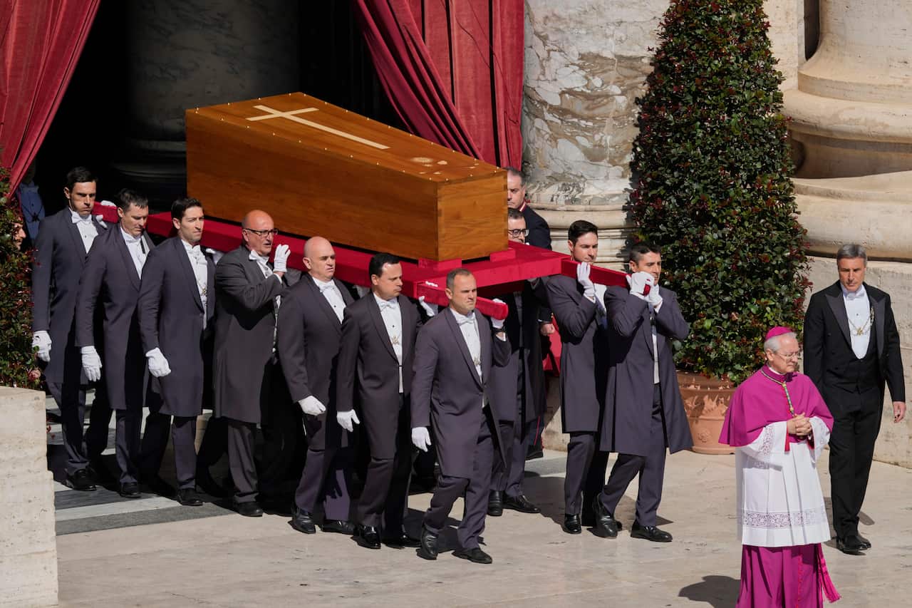 Pallbearers in formal morning suits and white gloves carry the cypress wood coffin of Pope Francis out of St Peter's Basilica during his funeral service.