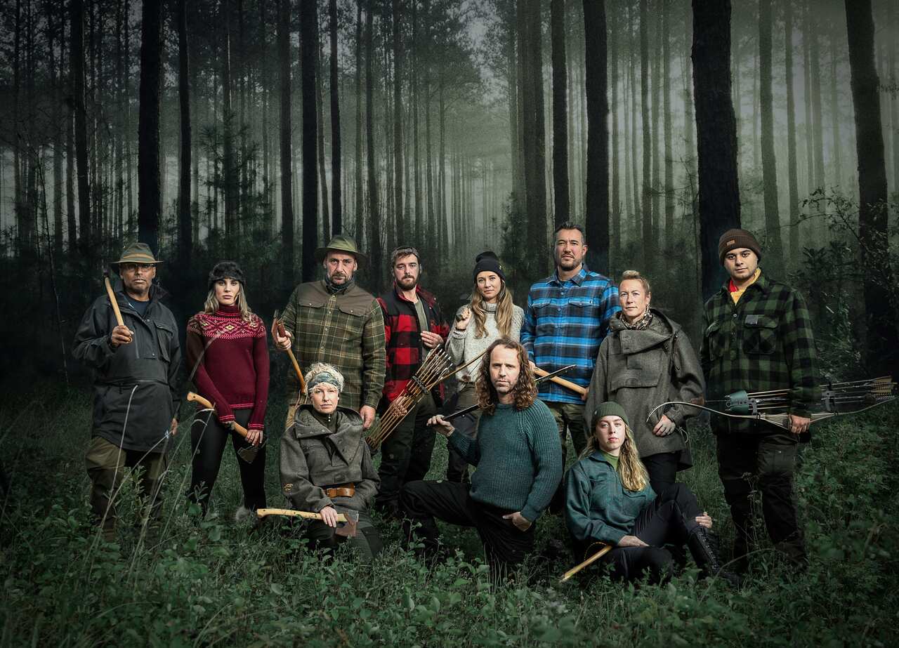 A group of people pose in the forest holding axes, bow and arrows