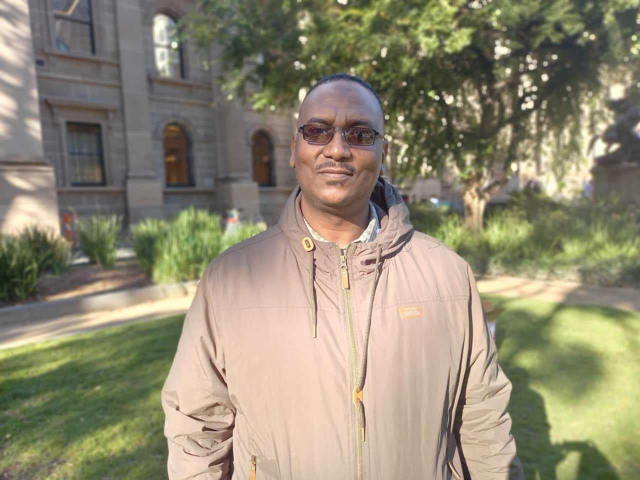 A man in sunglasses stands in the park and faces the camera