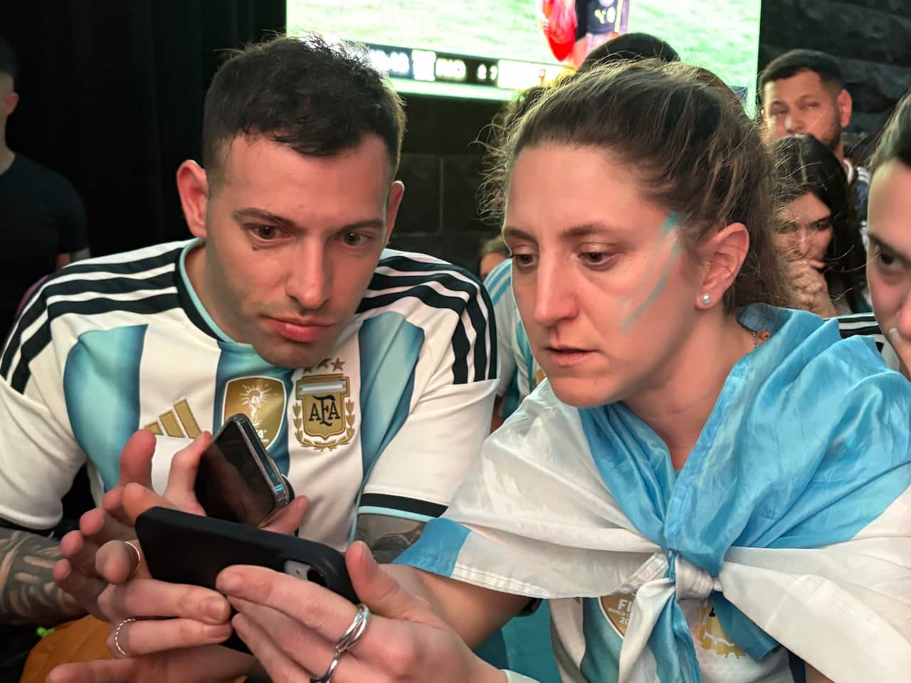 A photo of two Argentina fans watching the World Cup 2026 final on their phone at a live site in Sydney.