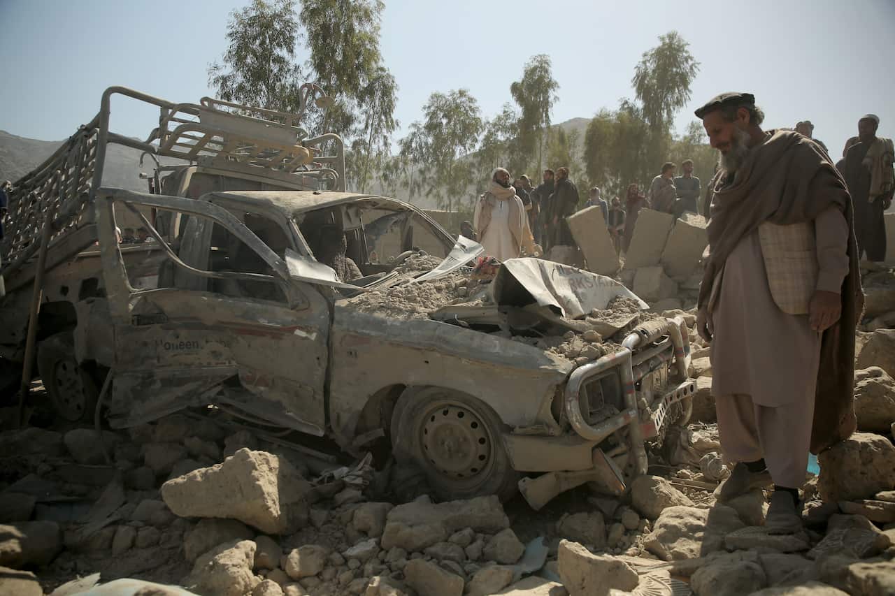 A group of people observing rubble near a heavily damaged car.