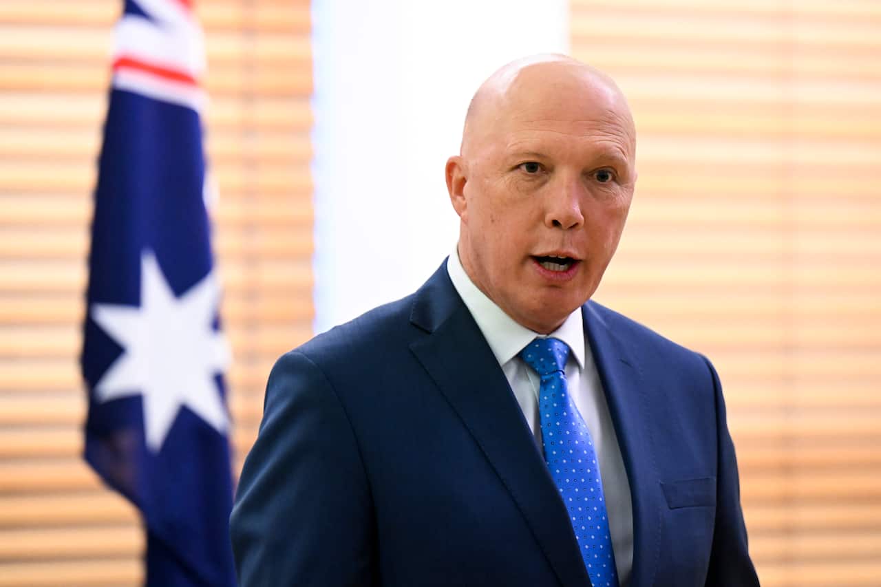 Peter Dutton standing inside. An Australian flag is behind his right shoulder