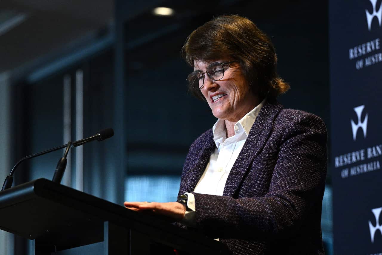 A woman in a blue suit delivering a speech in front of a blue poster