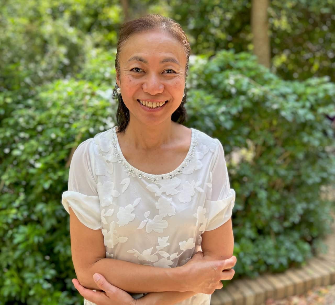A woman in a white shirt sitting in a garden with her arms folded.