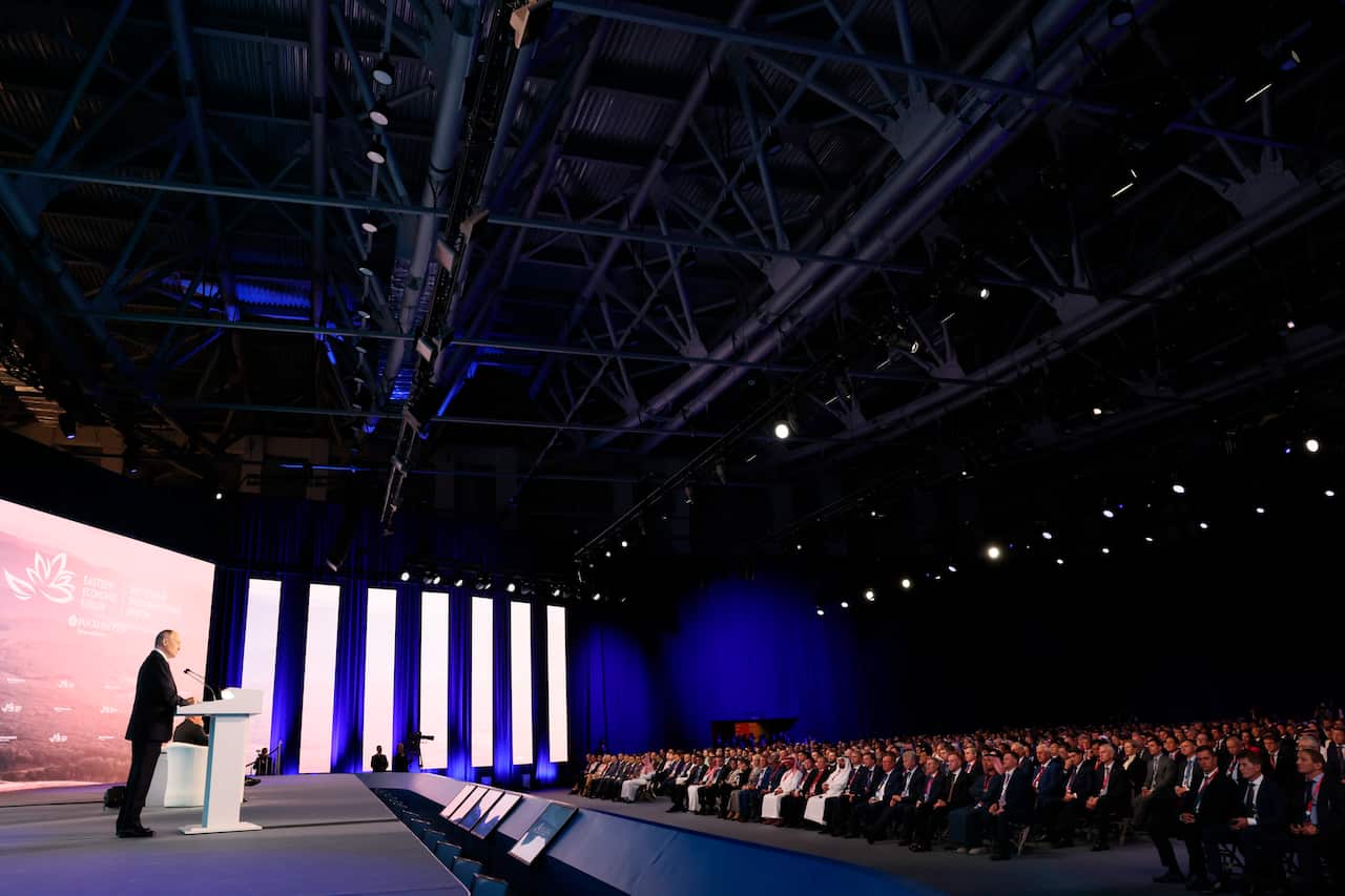 A man standing on a stage in front of a lectern and speaking in front of a microphone.