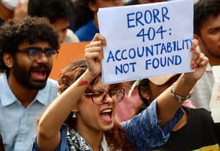 A student holds up a sign as she opens her mouth to shout a slogan with her eyes closed