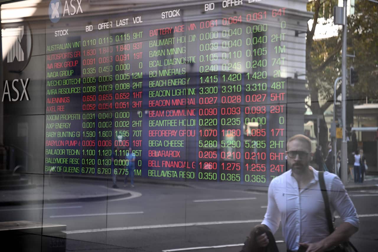 A reflection of a person walking past a light up stock exchange sign.