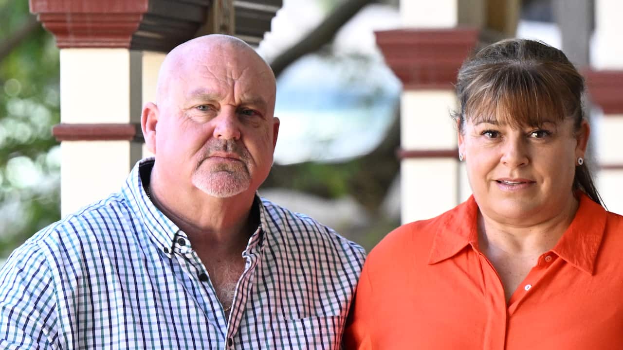 A man wearing a checked shirt, standing next to a woman wearing an orange blouse.
