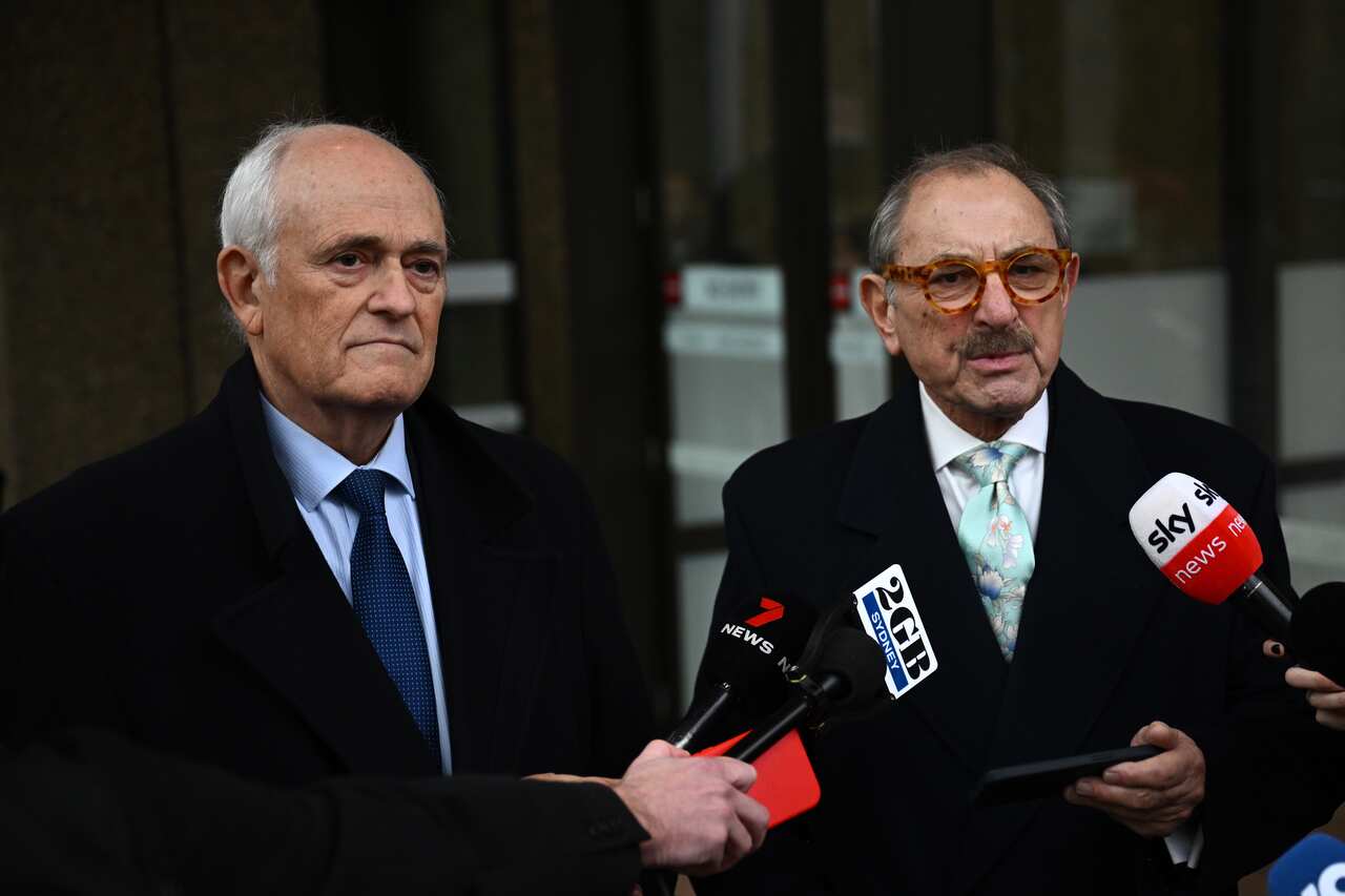 Two men in suits are speaking to the media.