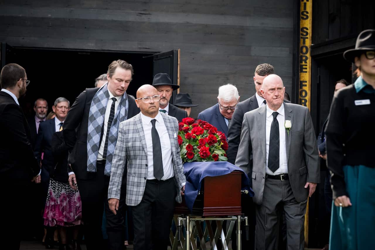 Pallbearers carrying a casket with an Australina flag and roses draped on top of it.