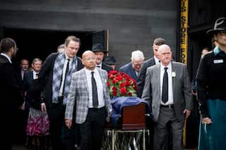 Pallbearers carrying a casket with an Australina flag and roses draped on top of it.