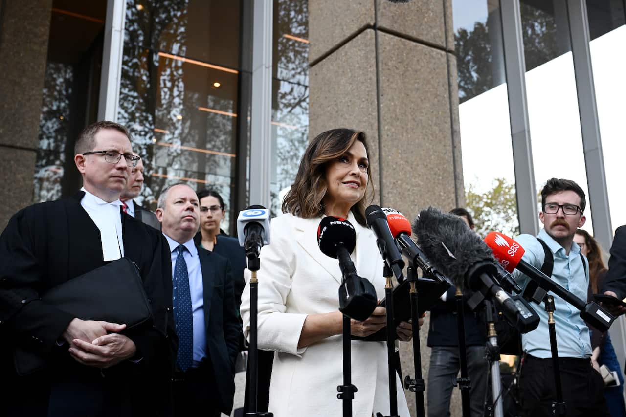 Lisa Wilkinson outside court surrounded by media and supporters, with microphones in front of her.