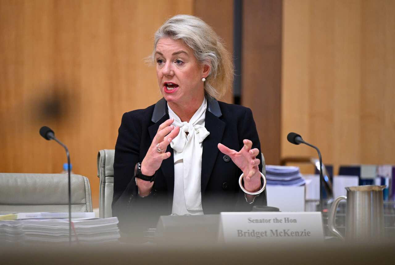 A woman wearing formal attire speaks while seated at a desk in front of a microphone.