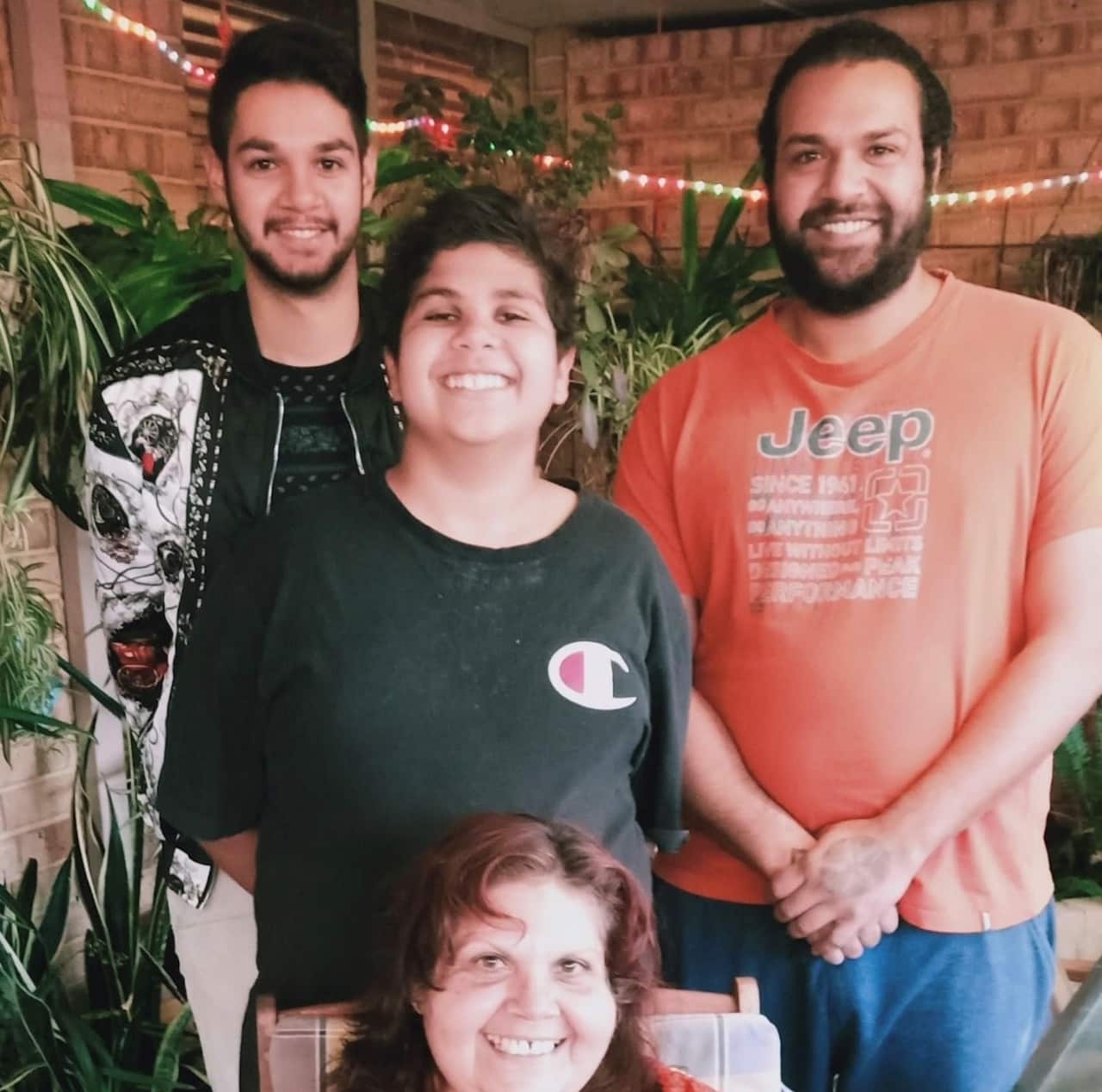 Cassius Turvey, centre, wearing a black t-shirt and big smile, behind his mother Mechelle, and standing between two other smiling men.