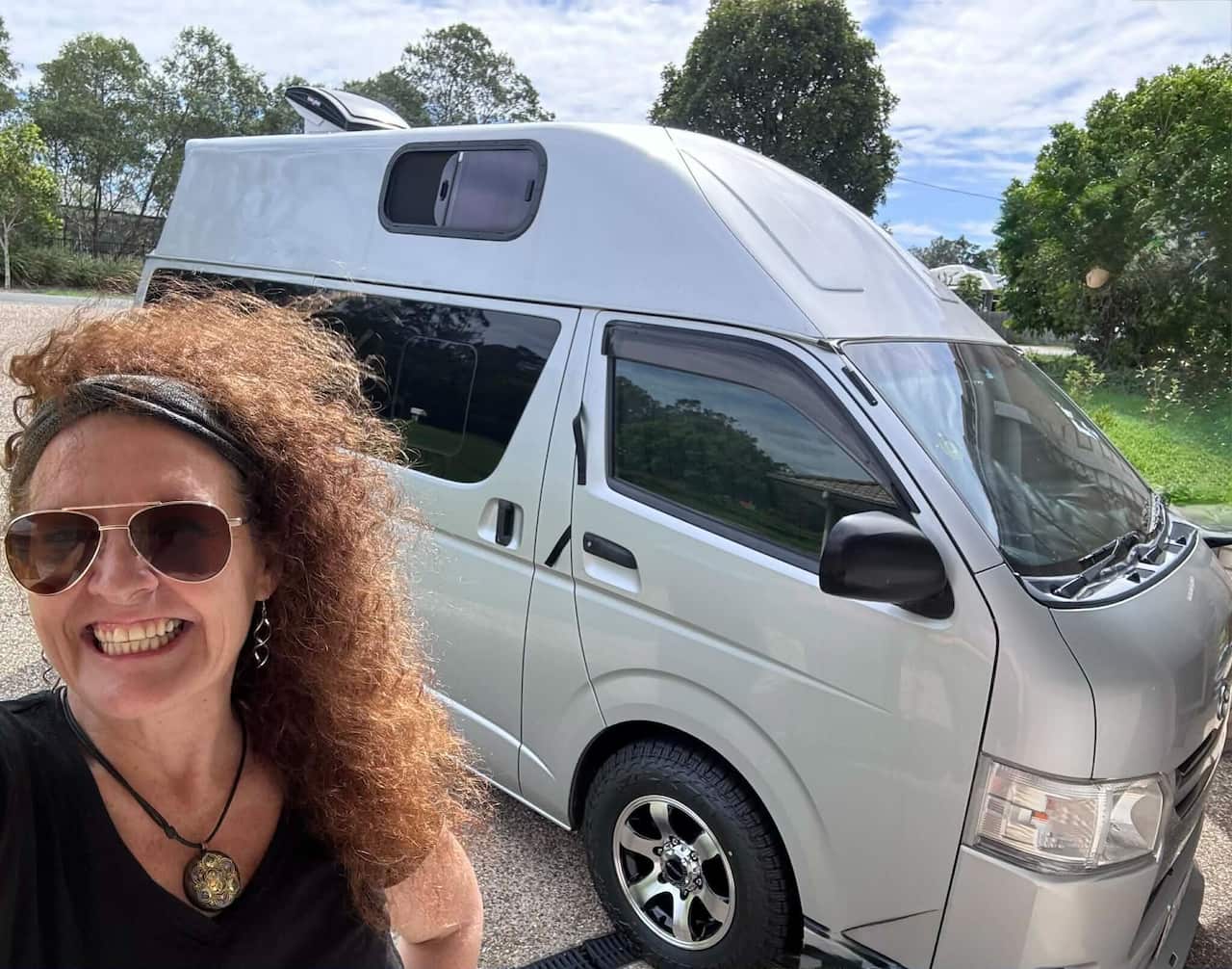 A woman smiling with her campervan.