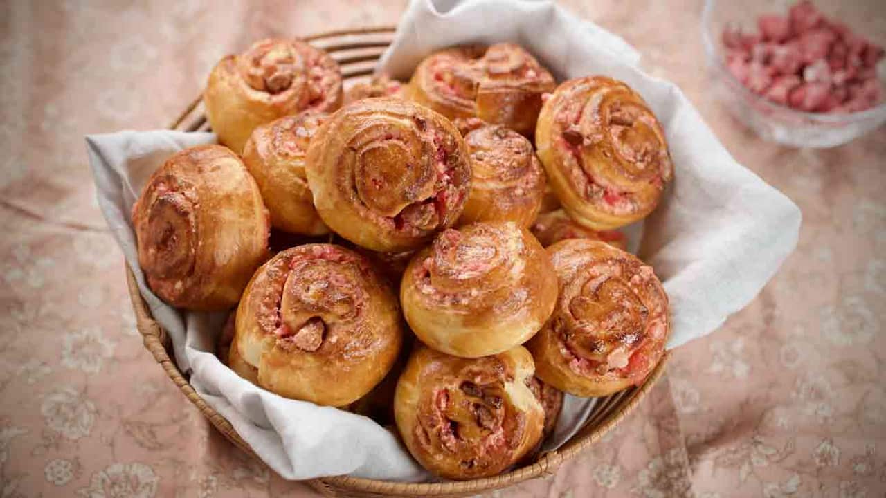 A basket lined with a white cloth holds a bounty of round brioche rolls studded with pink praline. 