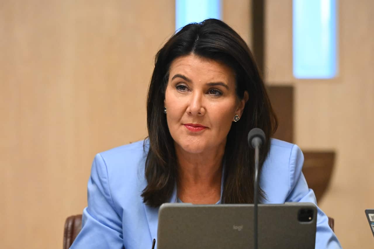 A woman in a light blue jacket sits at a laptop