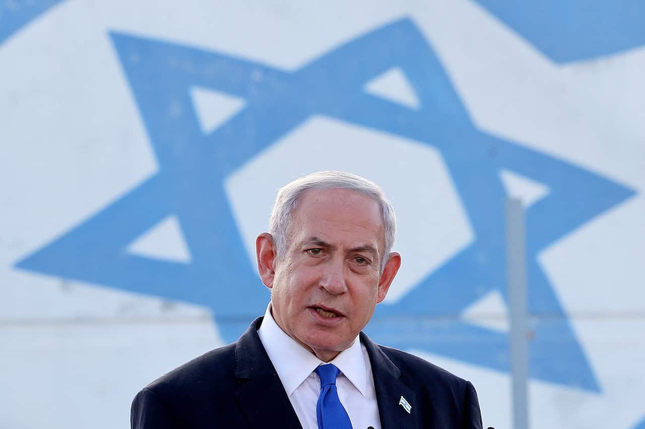 A man speaking in front of a large blue Star of David symbol.