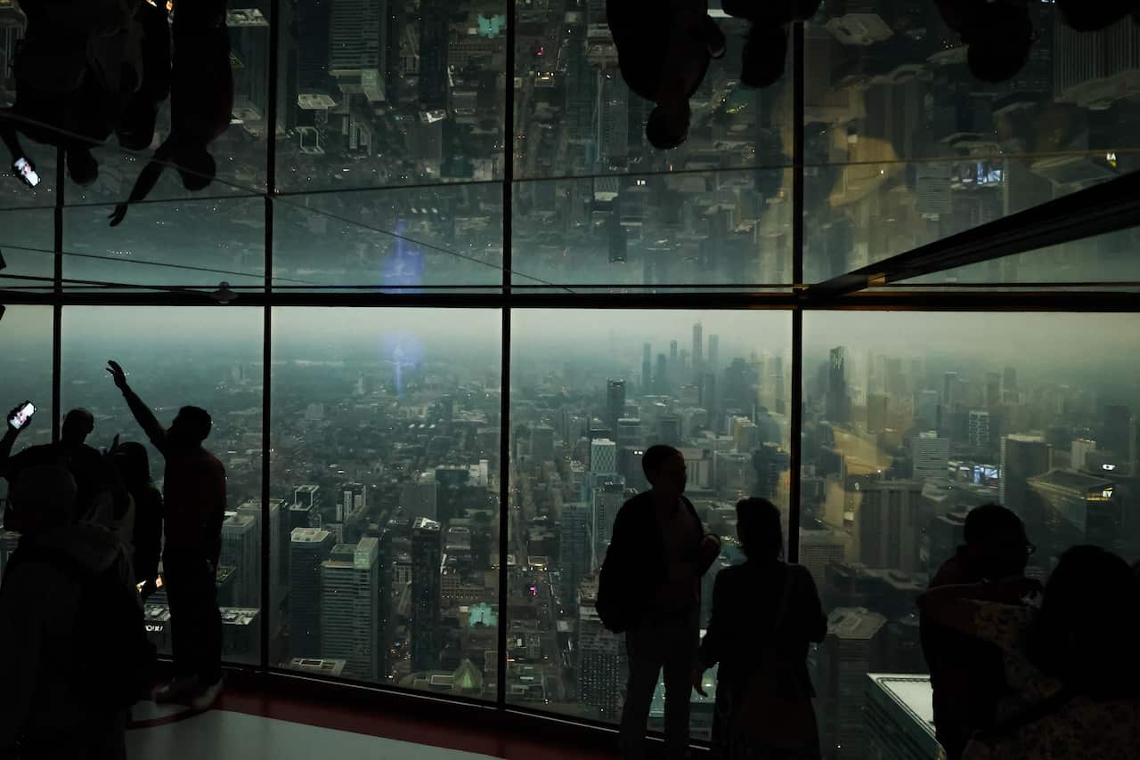 People look out from glass windows as smoke from wildfires blankets the city.