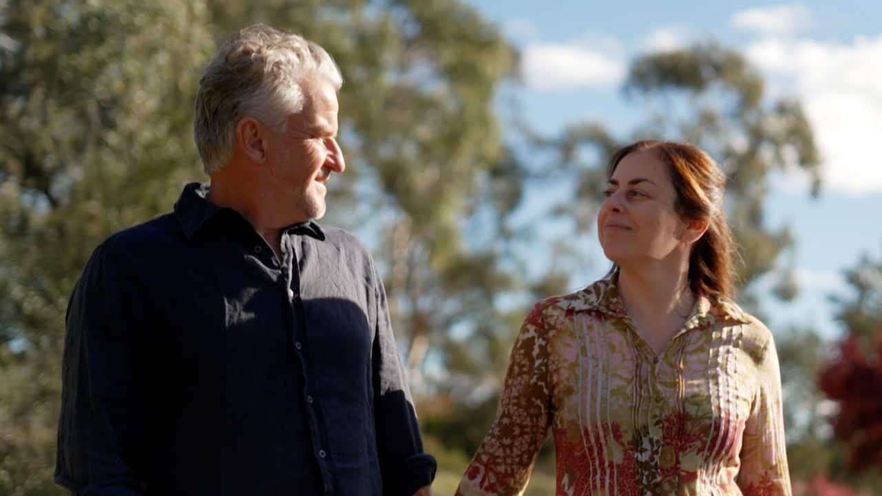 a middle aged man and woman holding hands walking outside on a sunny day