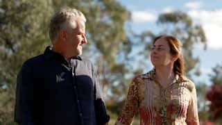 a middle aged man and woman holding hands walking outside on a sunny day