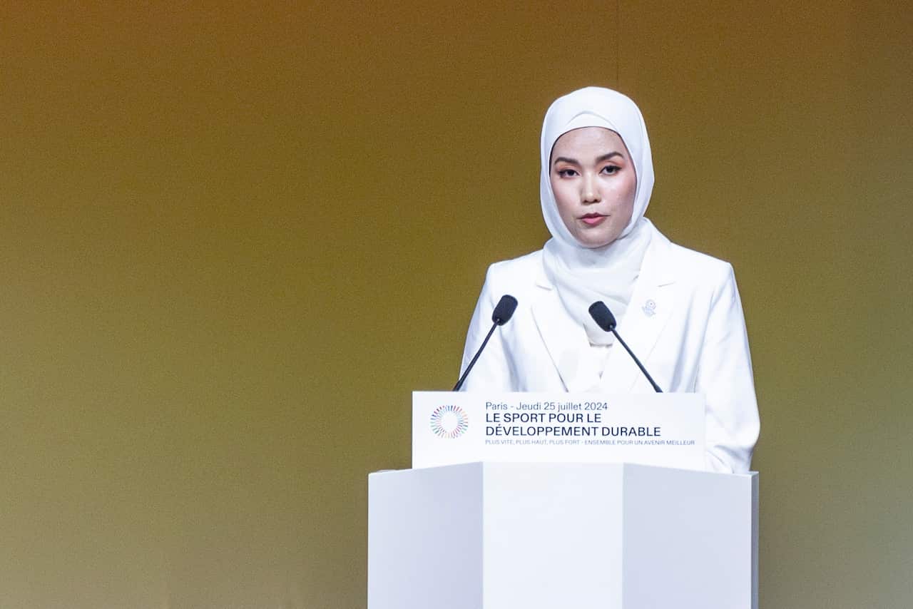 A woman wearing a head scarf speaks on a podium.
