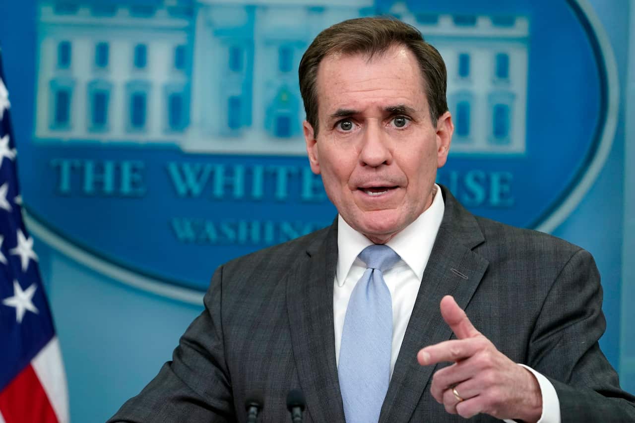A man in a suit points while standing in front of the White House logo