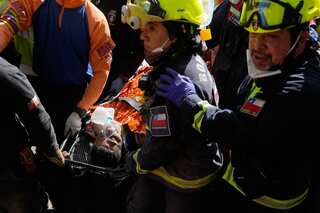A man lies on a stretcher wearing an oxygen mask. He is surrounded by first responders wearing yellow helmets who have rescued him.