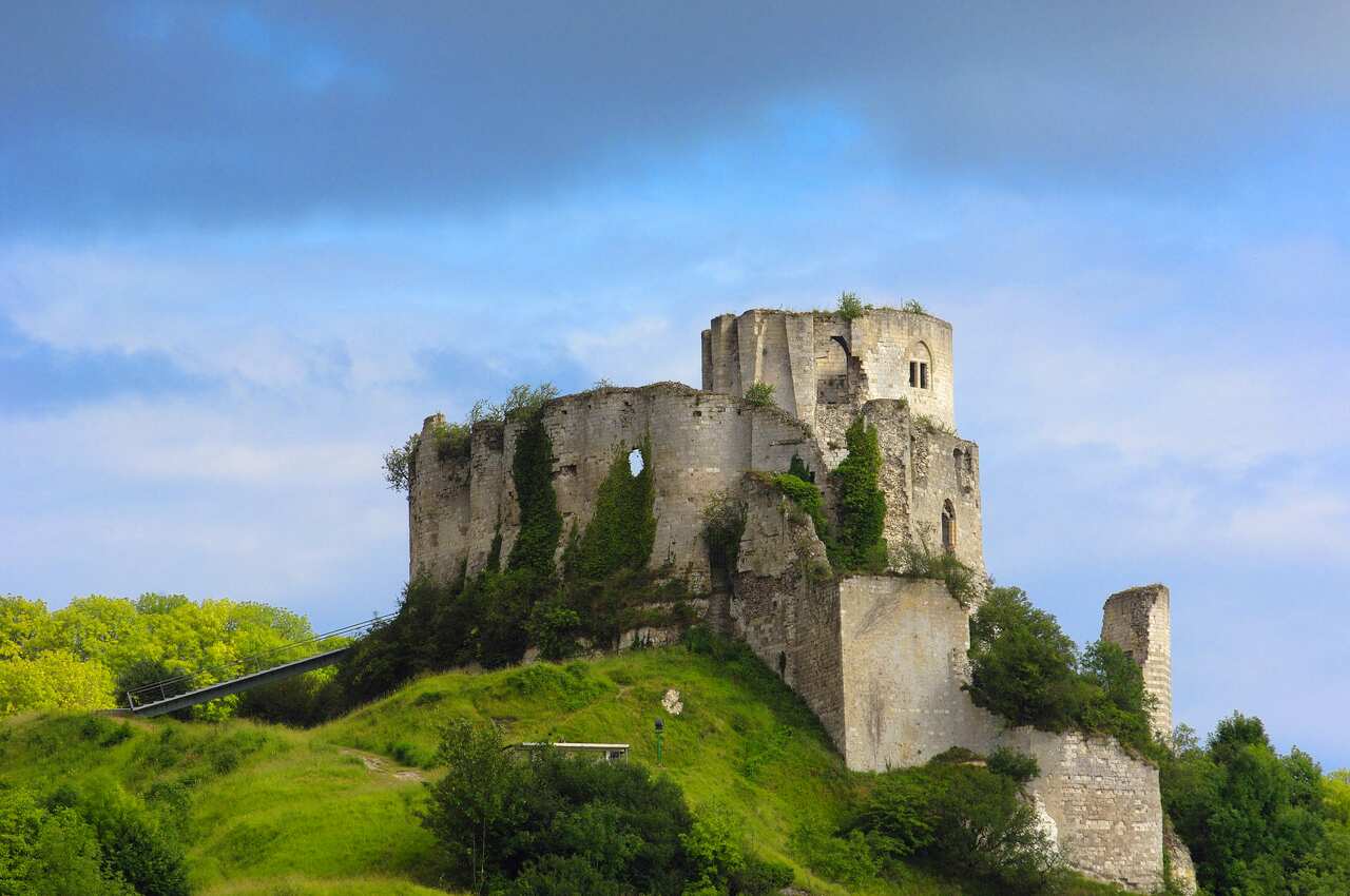 Ruins of a medieval castle sit on top of a grassy hill.