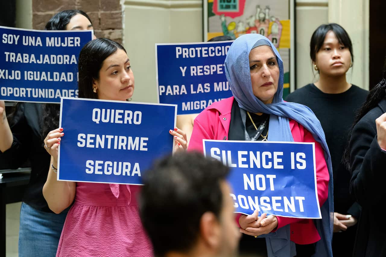 Women holding blue protest signs in different languages