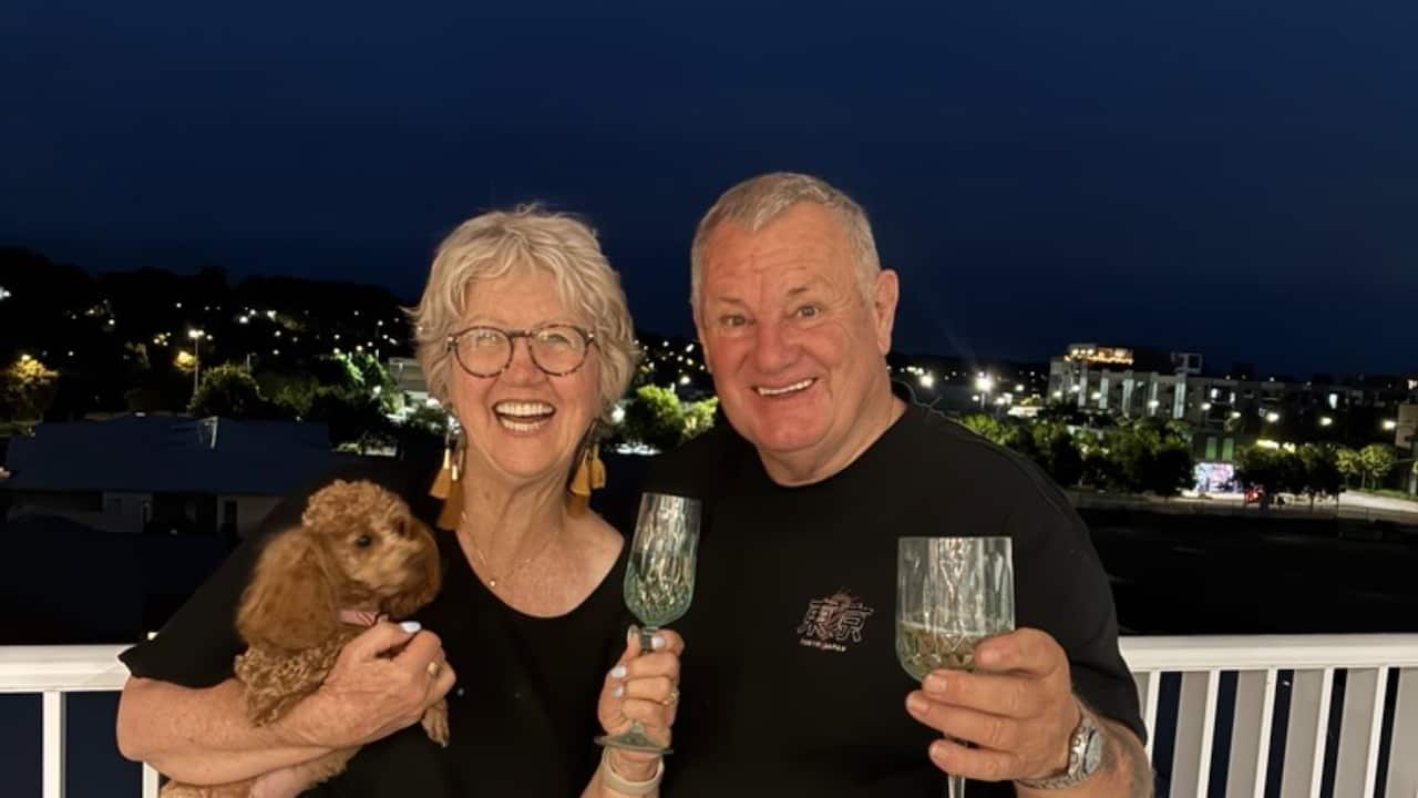 a middle aged woman and man holding wine glasses and a dog smiling at night time