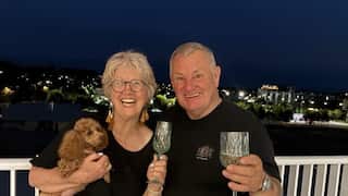 a middle aged woman and man holding wine glasses and a dog smiling at night time