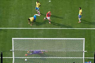 A goalkeeper wearing purple lunges for a football, as other players crowd around the goal net.